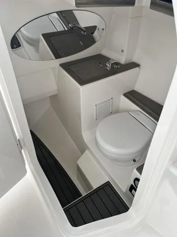 Slide: The Image of 2022 Edgewater 262CX boat interior with compact bathroom, featuring a toilet and sink. - 10
