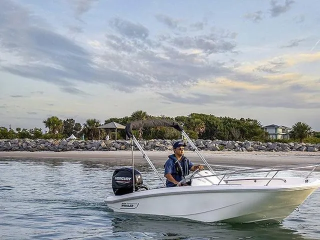 Slide: The Image of 2025 Boston Whaler 130 Super Sport boat cruising near a scenic shoreline. - 1