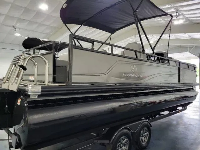 Slide: The Image of 2024 Regency 250 DL3 pontoon boat with canopy, displayed indoors on a trailer. - 4
