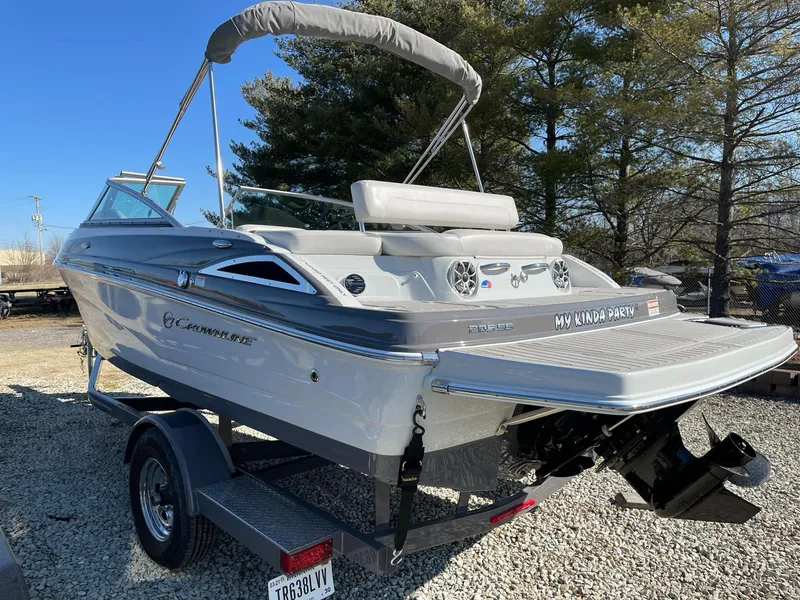 Slide: The Image of 2020 Crownline 205 SS boat on trailer, parked outdoors, with trees in the background. - 2