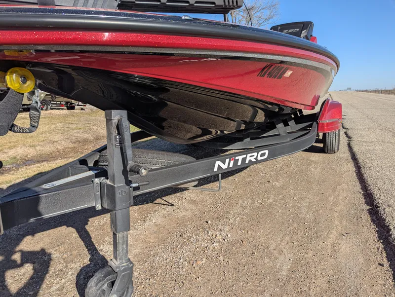 Slide: The Image of 2023 Nitro Z20 boat on trailer, red and black design, parked on gravel road. - 12