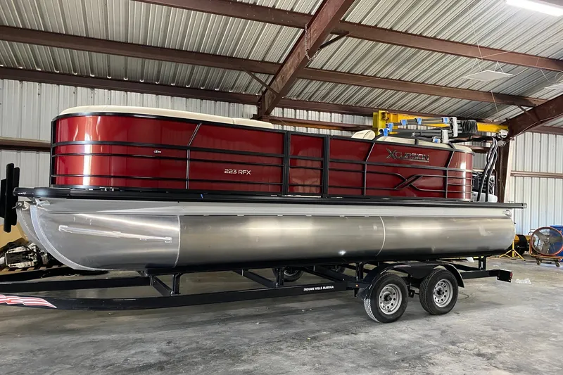 Slide: The Image of 2022 Xcursion 223 RFX pontoon boat in storage, featuring a sleek red design. - 1