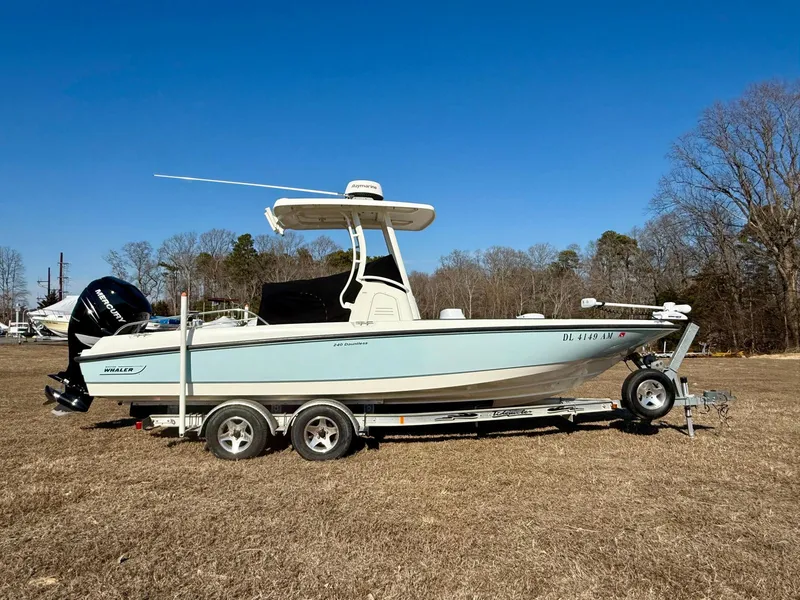 Slide: The Image of 2016 Boston Whaler 240 Dauntless boat on trailer, parked on grass under clear blue sky. - 1