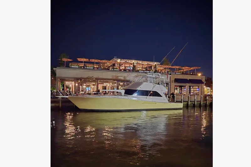 Slide: The Image of 1999 Viking 55 yacht docked at night near a lit waterfront restaurant. - 0