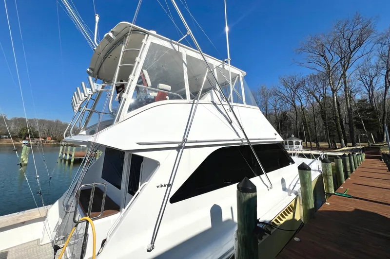 Slide: The Image of 1999 Viking 55 yacht docked by a serene lake under a clear blue sky. - 6