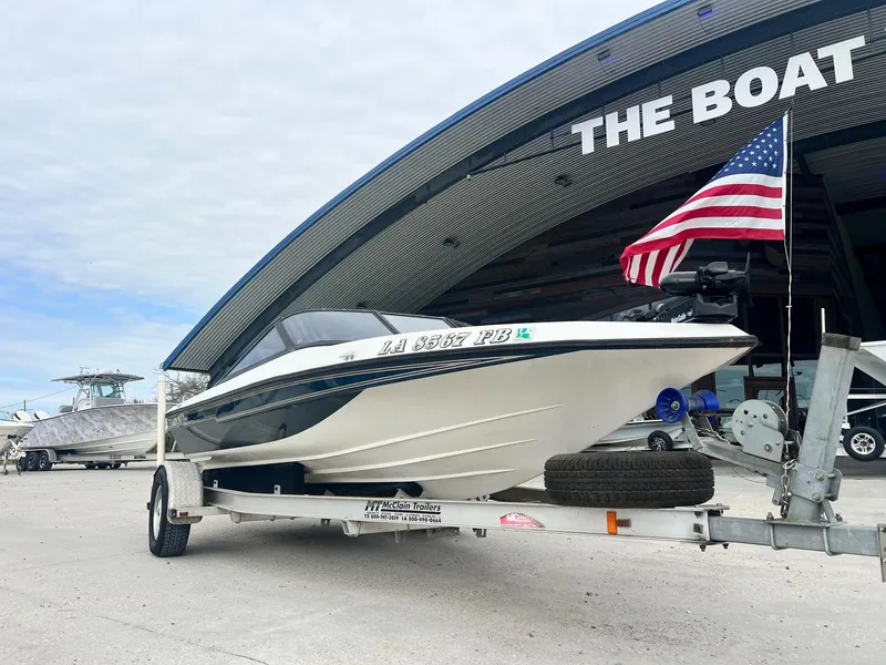 Slide: The Image of 1999 Champion 181 Elite boat on trailer with American flag, parked outside a boat dealership. - 2