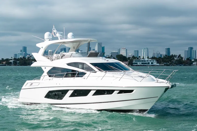 Slide: The Image of 2016 Sunseeker Manhattan 65 yacht cruising on open water with city skyline backdrop. - 16