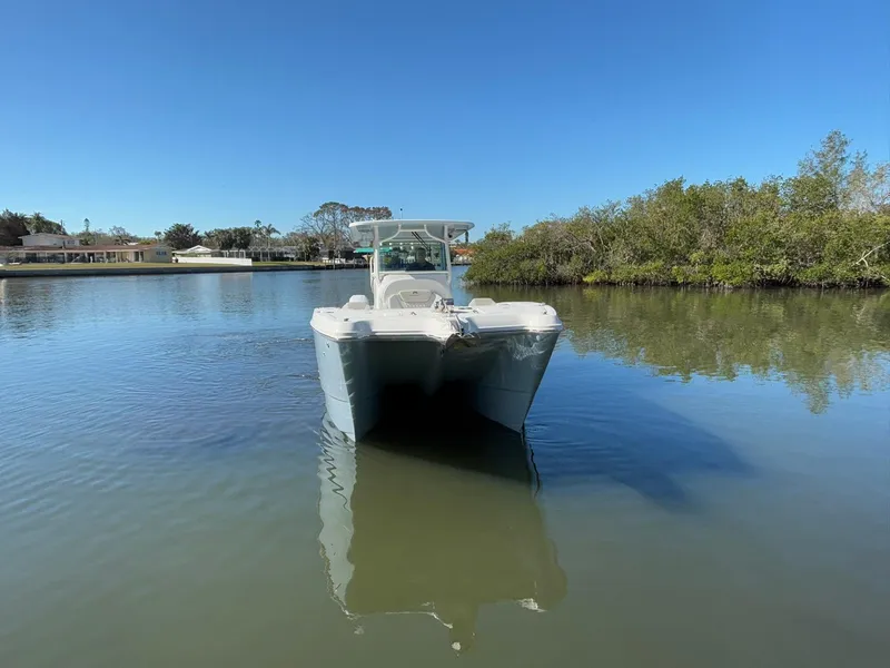 Slide: The Image of 2025 World Cat 325 CC boat on calm water, surrounded by trees and clear blue sky. - 2