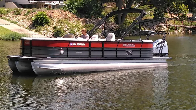 Slide: The Image of 2022 Xcursion 243RFX pontoon boat cruising on a calm lake. - 1