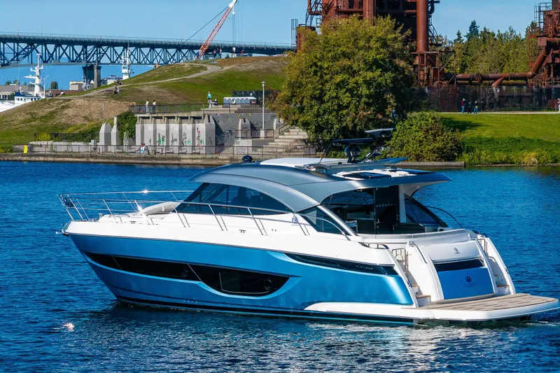 Slide: The Image of 2025 Riviera 4600 Sport Yacht cruising on a scenic waterway near industrial structures. - 18