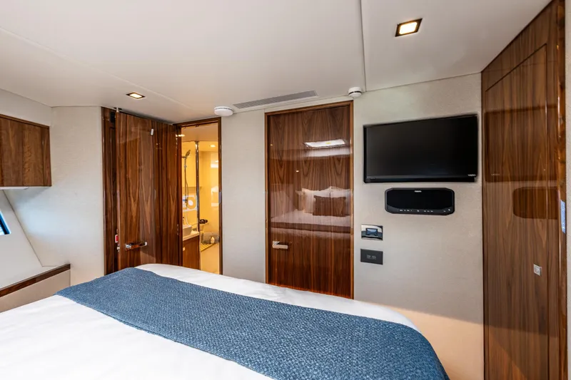 Slide: The Image of Luxurious interior of 2025 Riviera 4600 Sport Yacht bedroom with TV and ensuite bathroom. - 45