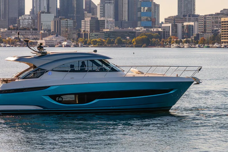 Slide: The Image of 2025 Riviera 4600 Sport Yacht cruising near city skyline on a sunny day. - 58