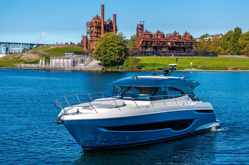 Slide: The Image of 2025 Riviera 4600 Sport Yacht cruising on a scenic river with industrial backdrop. - 59