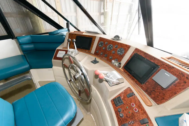 Slide: The Image of 1998 Bayliner 4788 Pilot House Motoryacht helm with blue seating and wood-accented dashboard. - 22