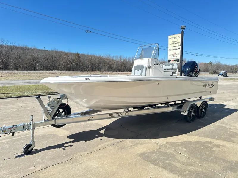 Slide: The Image of 2025 Robalo 226 Cayman boat on trailer, parked outdoors under clear blue sky. - 2
