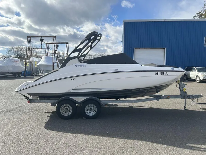 Slide: The Image of 2017 Yamaha Boats 212 Limited S on trailer, parked outdoors near blue building. - 10