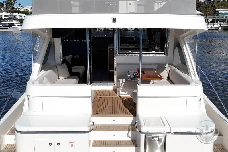 Slide: The Image of 2026 Riviera 58 Sports Motor Yacht, elegant deck view with seating and table, docked by the water. - 19