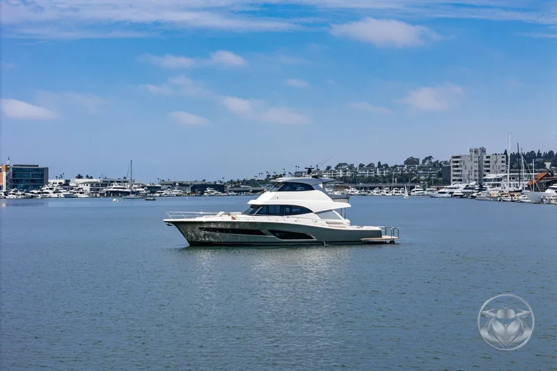 Slide: The Image of 2025 Riviera 64 Sports Motor Yacht on calm waters, cityscape in background. - 61