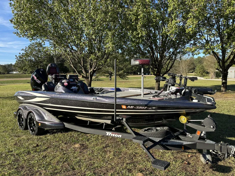 Slide: The Image of 2016 Triton 21 TrX Patriot boat on trailer, parked on grass with trees in background. - 11