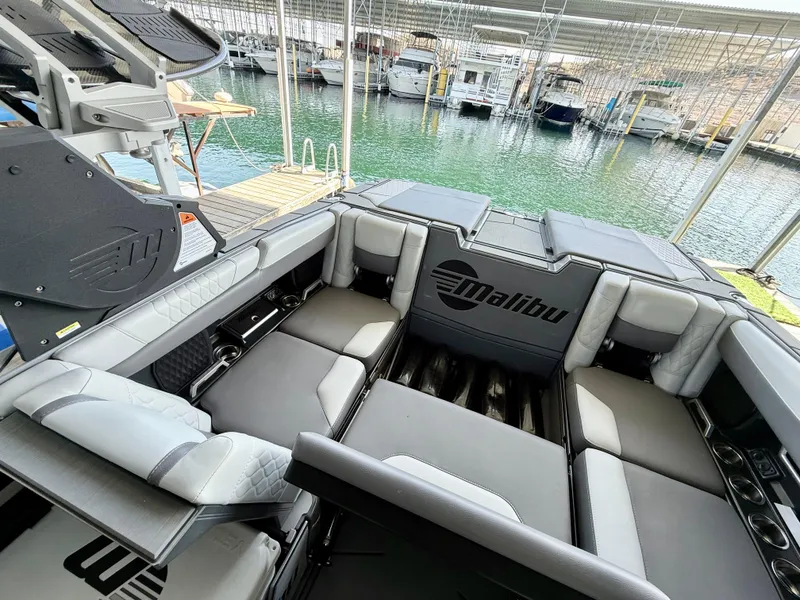 Slide: The Image of 2021 Malibu M240 boat interior with spacious seating, docked at a marina. - 21