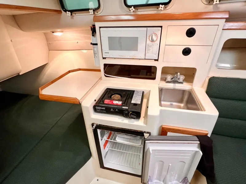 Slide: The Image of Compact kitchen area in a 2000 Albin 28 Tournament Express boat, featuring a microwave, sink, and mini-fridge. - 14
