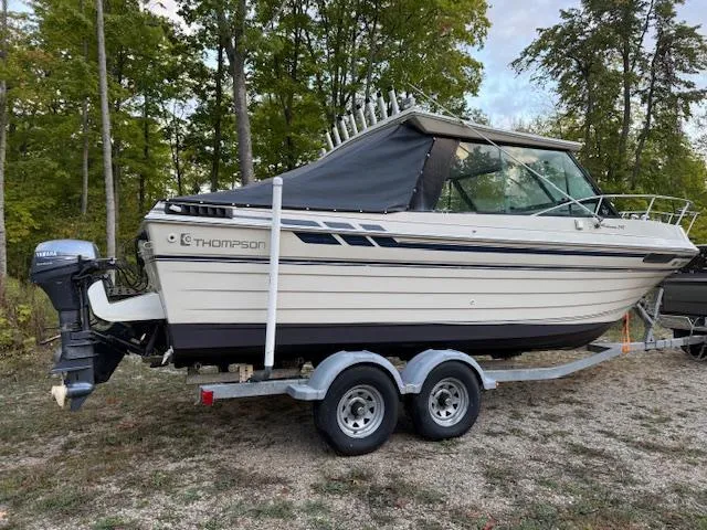 Slide: The Image of 1990 Thompson 240 Fisherman boat on trailer, parked outdoors with trees in the background. - 5