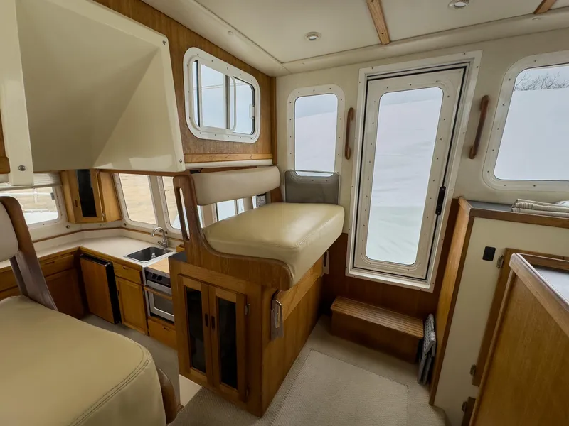 Slide: The Image of Interior of 2006 Nordic Tug 32' Plus, featuring kitchen and seating area with large windows. - 13