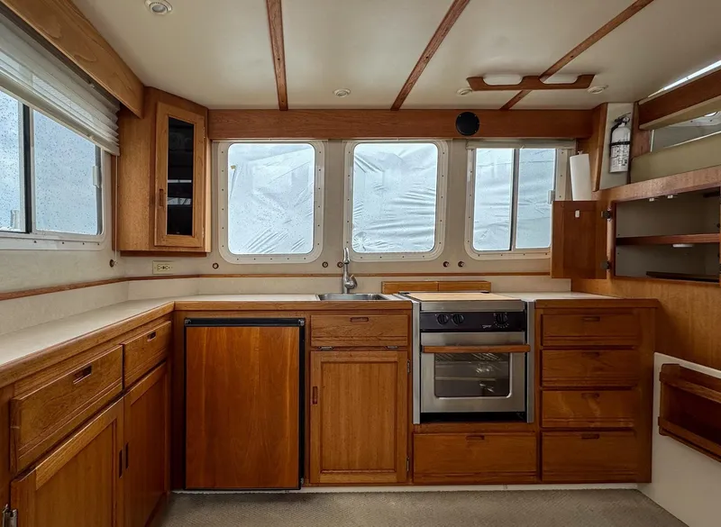 Slide: The Image of 2006 Nordic Tug 32' Plus kitchen with wooden cabinets, stove, and large windows. - 2