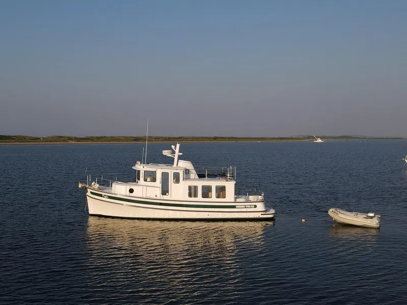 Slide: The Image of 2006 Nordic Tug 32' Plus boat anchored on calm water with a small dinghy nearby. - 23