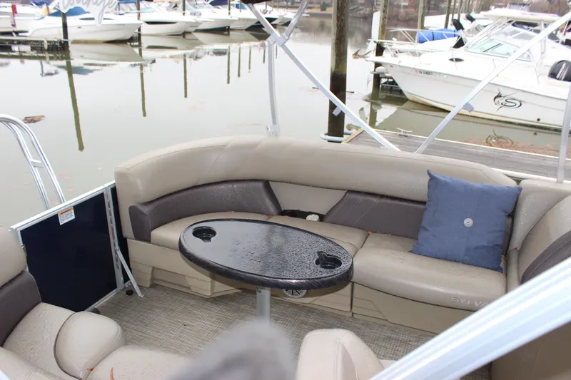 Slide: The Image of 2023 Sylvan Mirage 820 LZ boat interior with seating and table, docked at marina. - 11