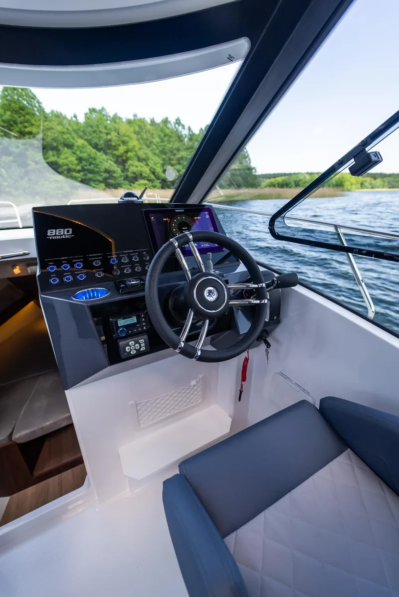 Slide: The Image of 2025 Nautic 880 boat cockpit with modern steering and control panel on a scenic lake. - 16