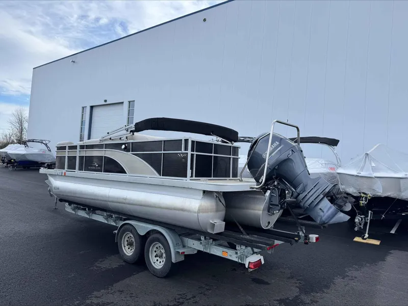 Slide: The Image of 2016 Bennington 22SLXP pontoon boat on trailer, parked outside a large building. - 1
