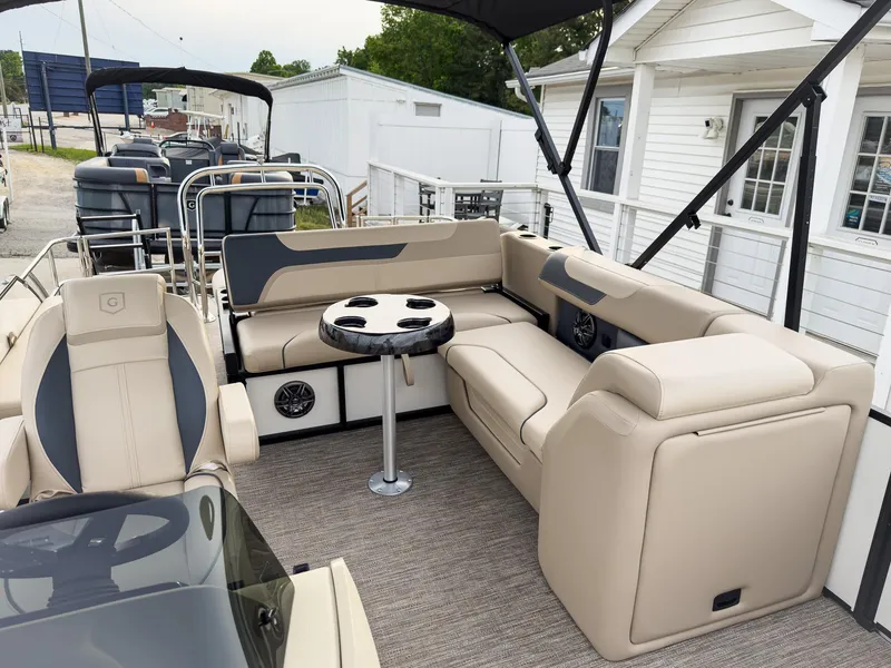 Slide: The Image of 2025 Godfrey Sweetwater 22' Tritoon with luxurious seating and table, docked near white building. - 10