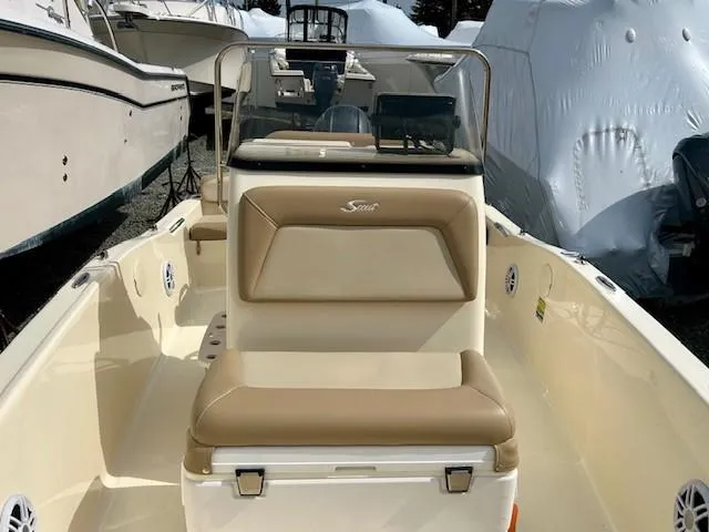 Slide: The Image of 2023 Scout 175 Sportfish boat with beige seating and console, docked among other boats. - 6