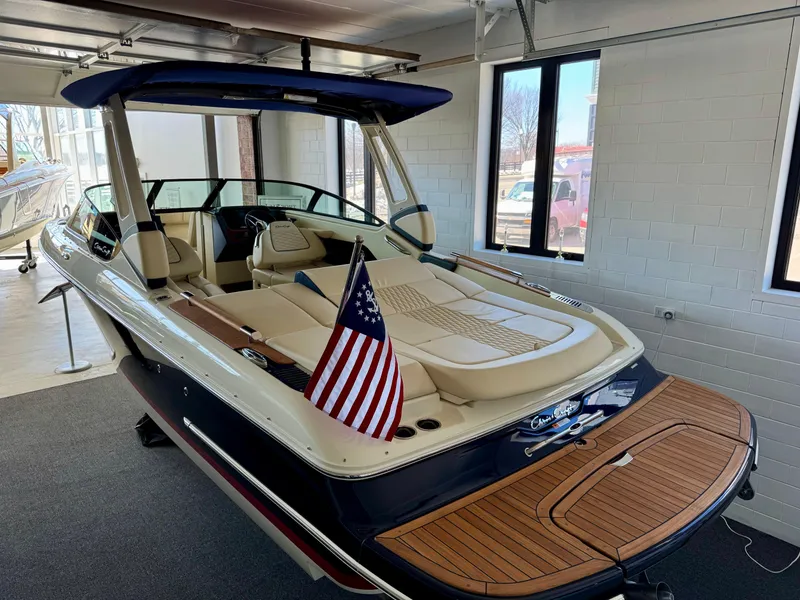 Slide: The Image of 2025 Chris-Craft Sportster 25 boat with American flag, displayed indoors. - 2