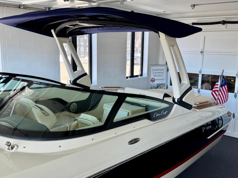 Slide: The Image of 2025 Chris-Craft Sportster 25 boat in showroom, featuring sleek design and modern canopy. - 28