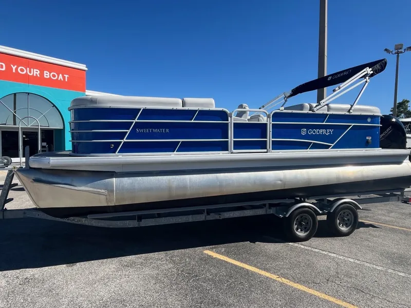 Slide: The Image of 2022 Godfrey SWEETWATER 2286 SFL pontoon boat on trailer, parked outdoors. - 2
