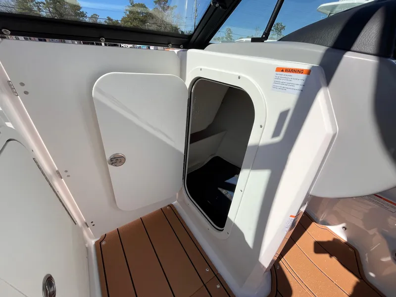 Slide: The Image of 2025 Chaparral 23 SSi OB boat interior storage compartment with open door, wood-textured flooring. - 13