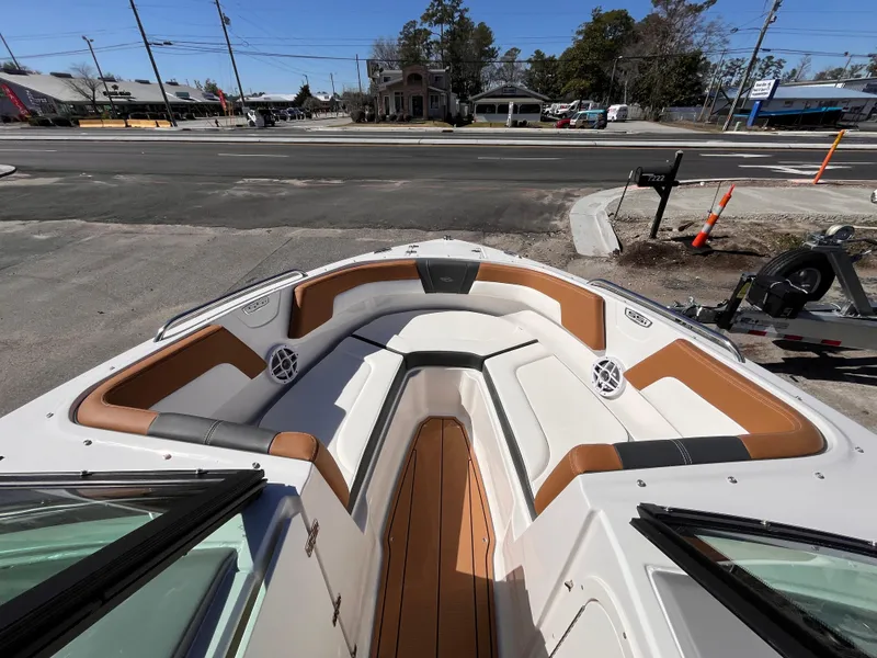 Slide: The Image of 2025 Chaparral 23 SSi OB boat interior with tan and white seating, docked near a road. - 14