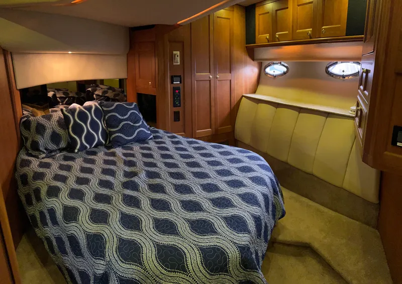 Slide: The Image of 2004 Cruisers Yachts 5000 Sedan Sport cabin with bed, wooden cabinets, and porthole windows. - 44