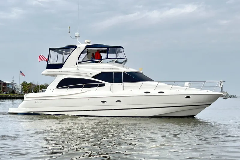 The Image of 2004 Cruisers Yachts 5000 Sedan Sport on calm water, featuring sleek design and American flag. - 0