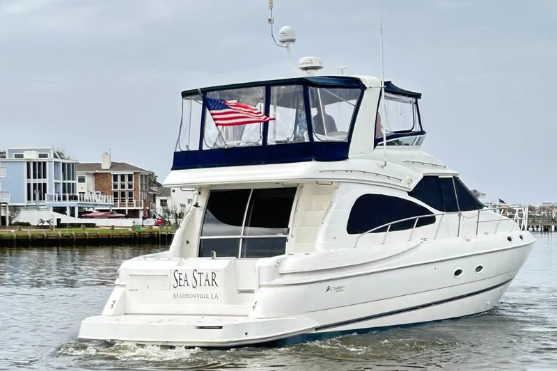 Slide: The Image of 2004 Cruisers Yachts 5000 Sedan Sport on water, American flag, residential backdrop. - 2