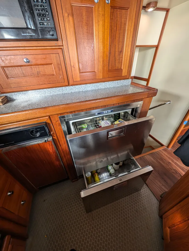 Slide: The Image of 2002 Nordhavn Trawler kitchen with open stainless steel drawer fridge, wooden cabinets, and microwave. - 11