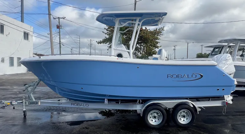 Slide: The Image of 2025 Robalo 232 Explorer boat in blue on a trailer, parked outdoors. - 4