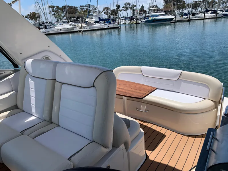 Slide: The Image of 2011 Sea Ray 330 Sundancer yacht interior with white seating and wooden table, docked at marina. - 21