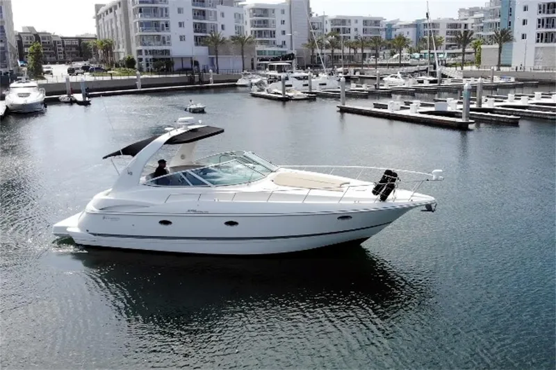 The Image of 2005 Cruisers Yachts 370 Express in marina, surrounded by modern buildings. - 0