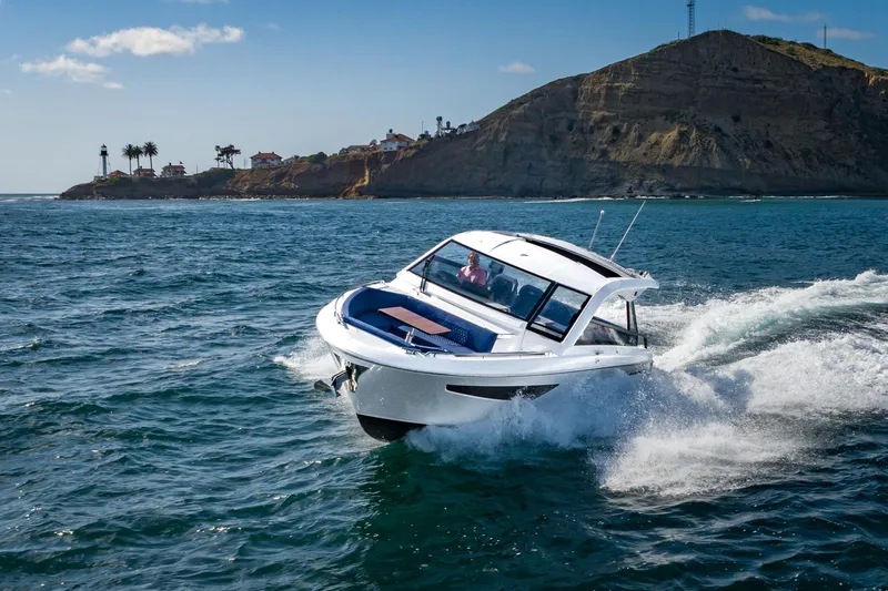 Slide: The Image of 2024 Bavaria Vida 33 boat cruising near a rocky coastline under a clear blue sky. - 17