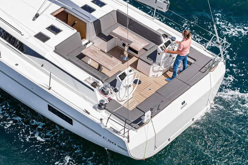 Slide: The Image of 2024 Bavaria C50 yacht sailing with a person at the helm, featuring spacious deck and seating. - 25