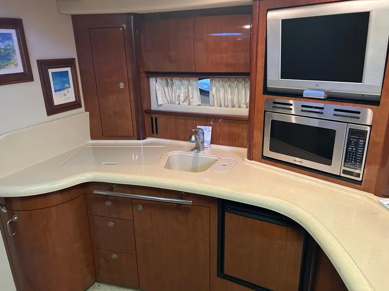 Slide: The Image of 2004 Sea Ray 420 Sundancer yacht kitchen with wood cabinetry, sink, microwave, and TV. - 19