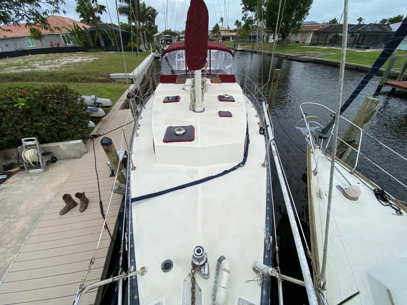 Slide: The Image of 1986 Bruce Roberts 43 Ketch docked by a canal, featuring a clean deck and red sail cover. - 7